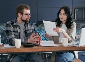 Young couple managing their finances with laptop and documents in a modern kitchen setting.